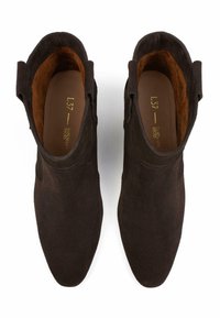 Stivali ankle in suede marrone con punta affusolata, dettagli di cucitura sottili e linguette laterali per una facile indossatura. Fodera interna morbida visibile.
