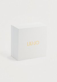 Valkoinen tekstuurinen suorakulmainen laatikko, jossa on kultainen "LIU·JO" -logo keskitettynä etupuolelle, taustanaan yksinkertainen valkoinen tausta.