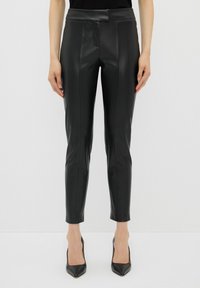 Zwarte leren broek met een aansluitend ontwerp, voorzien van een soepele textuur, subtiele voornaaddetails en enkelhoogte. Gecombineerd met spitse zwarte hakken.