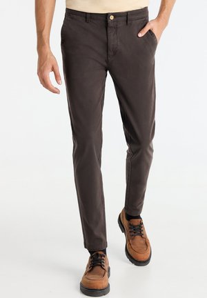 Brown cotton chinos with a slim fit, featuring a button closure, side pockets, and a smooth texture. Paired with brown lace-up shoes.
