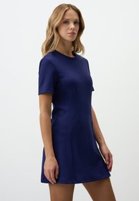 Navyblauwe jurk met korte mouwen van gladde stof, voorzien van een ronde halslijn en een licht uitlopende pasvorm met naden aan de voorkant.