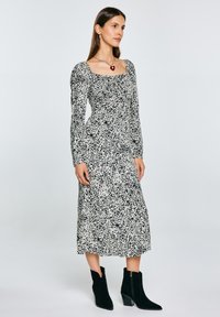 Abito midi a fantasia bianco e nero con scollo quadrato, maniche lunghe e tessuto texturizzato. Abbinato a stivaletti neri alla caviglia.