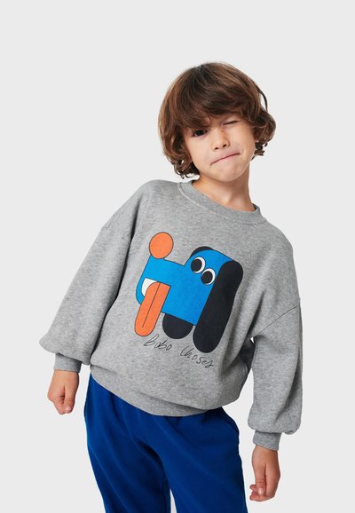 Felpa grigia con una grafica di un cane blu, dettagli arancioni e vestibilità ampia. Presenta polsini a coste e scollatura rotonda, abbinata a pantaloni blu.