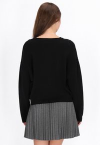 Pulover tricotat negru cu un guler larg, combinat cu o fustă pliată gri. Textura moale, designul simplu și croiala lejeră sunt evidente.