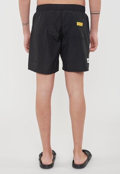 Pantaloni da nuoto neri realizzati in materiale leggero, con una vita elastica, una tasca laterale e un'etichetta distintiva sul retro.