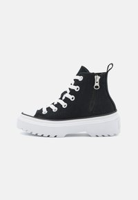 Czarne sneakersy typu high-top wykonane z kanwy, z białą gumową podeszwą, białymi sznurowadłami, bocznym zamkiem błyskawicznym i teksturowanym wierzchem.