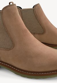 Stivaletti Chelsea in suede marrone con pannelli laterali elasticizzati, dettagli cuciti, punta arrotondata e suola in gomma. Texture liscia e design classico.