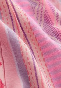 Gros plan d'un tissu doux avec des rayures roses et violettes, et des lignes de couture en pointillés formant un motif texturé à travers la surface.