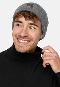 Gray knit beanie with a rectangular logo tag; black turtleneck sweater with ribbed collar, featuring a tight fit and smooth texture.