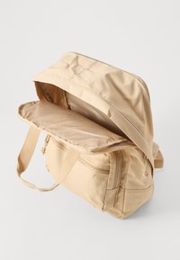 Beige tygväska med dragkedjestängning, har en platt, rymlig interiör och två sidofickor. Inkluderar en överdel med lock och justerbara axelremmar.