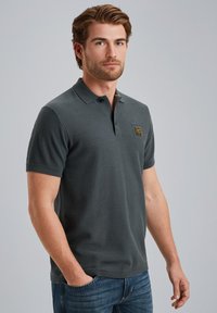 Mørkegrå polo t-shirt med korte ærmer, tekstureret stof og et lille vævet mærke på brystet. Kombineret med blå jeans.