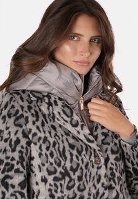Abrigo de mezcla de lana con estampado de leopardo y un collar de plumas gris, con un diseño de doble botonadura y detalles de cremallera dorados. Textura suave.