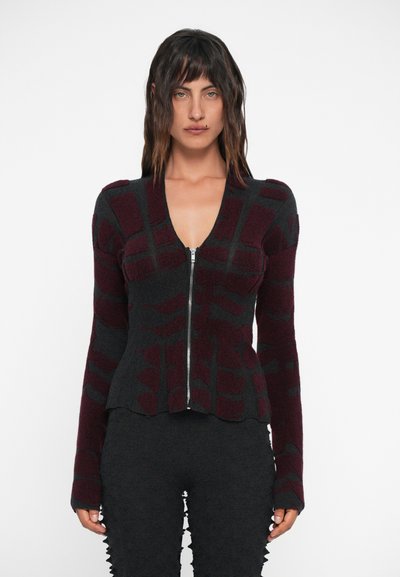 Bordeaux und dunkelgraue Reißverschlussjacke mit strukturiertem Muster, taillierte Passform und langen Ärmeln, getragen über einem passenden dunklen Outfit.