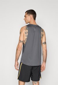 Grå atletisk tanktop med rund halsudskæring, ærmeløs design og diskrete detaljer på ryggen, parret med sorte shorts med gule accenter.