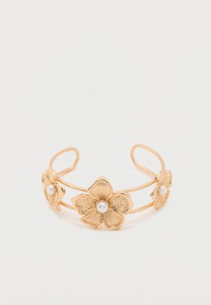 Bracelet manchette en or avec trois motifs floraux texturés, chacun orné d'une perle blanche centrale, présenté sur un fond blanc uni.