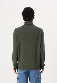 Pull à col roulé vert en tricot avec une coupe décontractée, des poignets et un ourlet côtelés. Le tissu a une texture douce et un design classique.