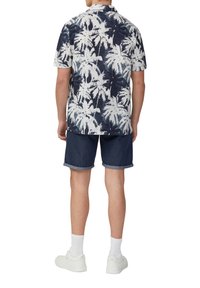 Korte mouwen overhemd met een blauw-wit palmbomenpatroon, gecombineerd met donkerdenim shorts en witte sneakers met opgerolde boorden en witte sokken.