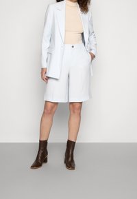 Lichtblauwe op maat gemaakte blazer gecombineerd met bijpassende knielange shorts. Beige aansluitend top, bruine enkellaarsjes met een chunky hak. Glad, gestructureerd materiaal.