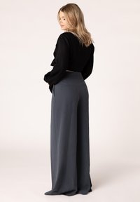 Zwart cropped top met lange mouwen, gecombineerd met grijze broek met wijde pijpen, voorzien van een aansluitende tailleband en achterzakken.