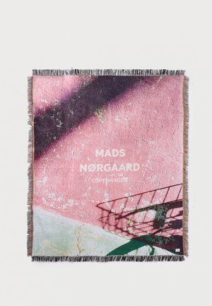 Szövött takaró, amelyen egy rózsaszín repedezett fal árnyékokkal és a "MADS NØRGAARD COPENHAGEN" felirat középen, bojtos szegélyek.