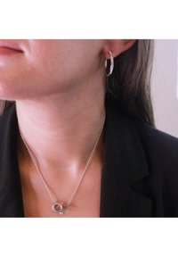 Orecchino a cerchio in argento con piccole pietre trasparenti e collana in argento con pendenti circolari intrecciati. Superfici lisce e lucide.