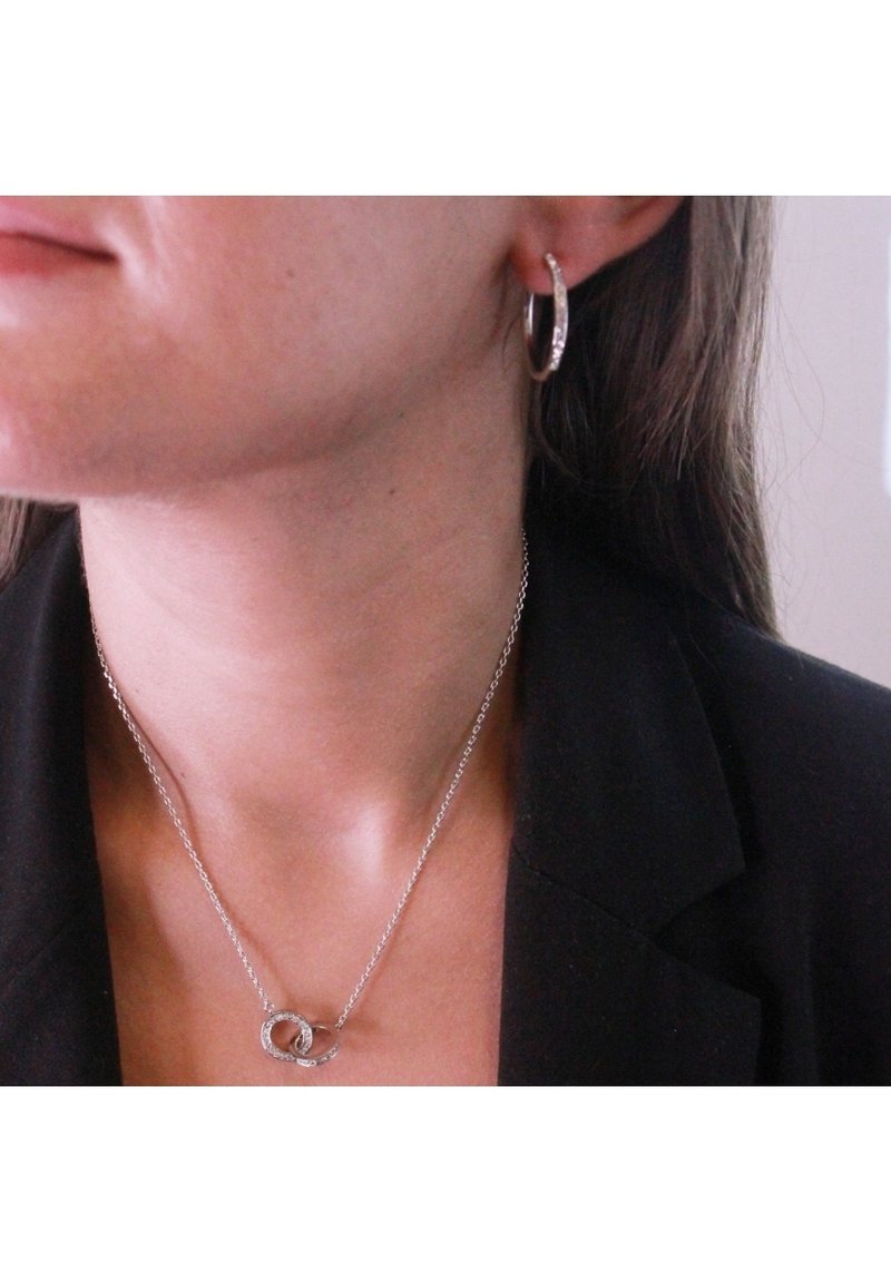 Orecchino a cerchio in argento con piccole pietre trasparenti e collana in argento con pendenti circolari intrecciati. Superfici lisce e lucide.
