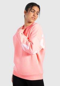 Sudadera rosa claro con puños y dobladillo acanalados, que presenta un gran diseño gráfico blanco en la manga y un logo en el pecho.