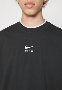 Svart bomullst-shirt med en vit Nike-logotyp och texten "AIR" centrerad på bröstet. Rund hals med vit kant. Slät textur.