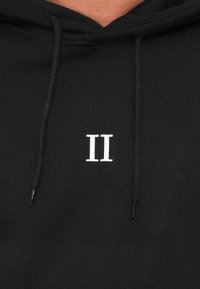 Sweat à capuche noir avec une poche avant, comportant une broderie blanche "II". Fabriqué en tissu doux avec des cordons de serrage et une finition texturée.