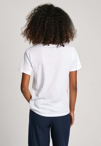 Camiseta de algodón blanca de manga corta y cuello redondo, combinada con pantalones azul marino a rayas, mostrando un ajuste relajado.