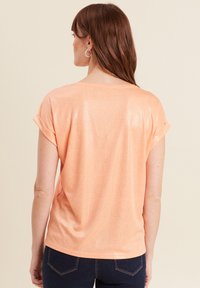 Korte mouwen, perzikkleurig top met een subtiele glans en een textuurpatroon, met omgeslagen mouwen en een losse pasvorm.