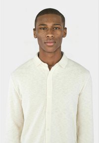 Lange mouwen blouse in off-white, gemaakt van gestructureerde stof. Heeft een kraag en een volledige knoopsluiting met zichtbare knopen.