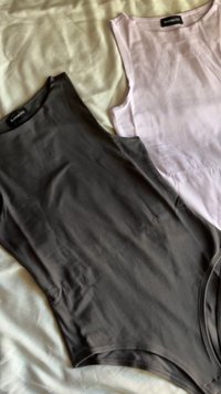 To flotte, ermeløse bodysuits, en i svart og den andre i lys rosa, med en tettsittende design og glatt, elastisk stoff.