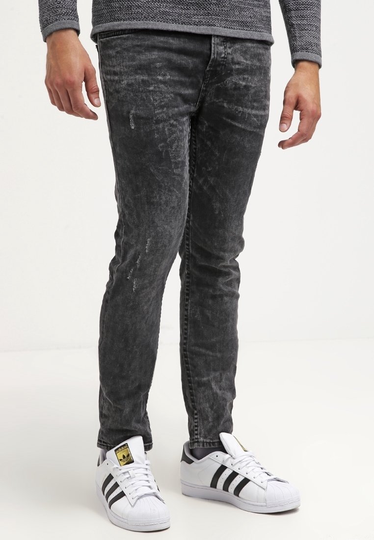 Black denim jeans with a faded texture and slight distressing, paired with white sneakers featuring black stripes and a textured sole.