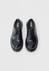 Pantofi negri din piele cu vârf rotund, design cu șireturi și talpă groasă din cauciuc cu crestături pentru aderență. Logo-ul este vizibil pe branț.