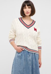 Kremowy sweter w splot warkoczowy z dekoltem w serek, z niebieskimi i czerwonymi paskami. Wyhaftowana litera "M". W połączeniu z dżinsową spódnicą.