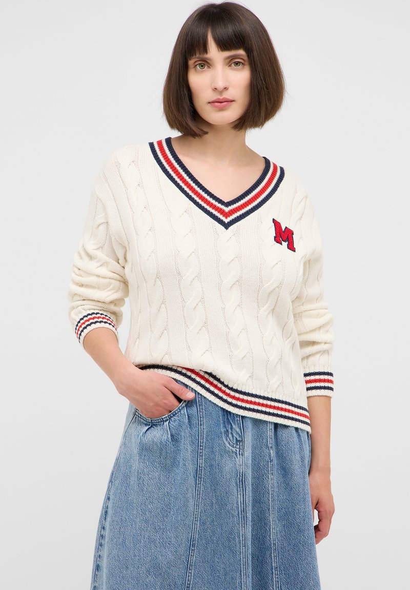 Kremowy sweter w splot warkoczowy z dekoltem w serek, z niebieskimi i czerwonymi paskami. Wyhaftowana litera "M". W połączeniu z dżinsową spódnicą.
