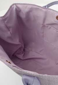 Borsa a spalla aperta con esterno intrecciato, interno in tessuto lilla, manici viola chiaro e una piccola tasca su un lato.