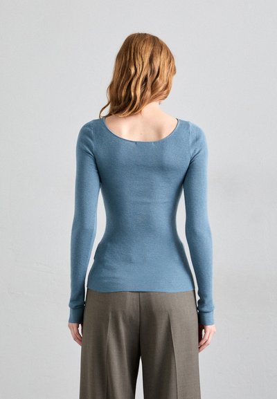 Top tricotat cu mânecă lungă, ajustat, de culoare albastru deschis, cu decolteu rotund și textură cu nervuri, asortat cu pantaloni gri cu talie înaltă.