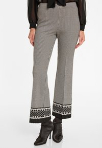 Schwarz-weiße Hahnentritt-Hosen mit ausgestelltem Schnitt und dekorativem gemustertem Saum, kombiniert mit schwarzen Stiefeletten. Glatte Stofftextur.