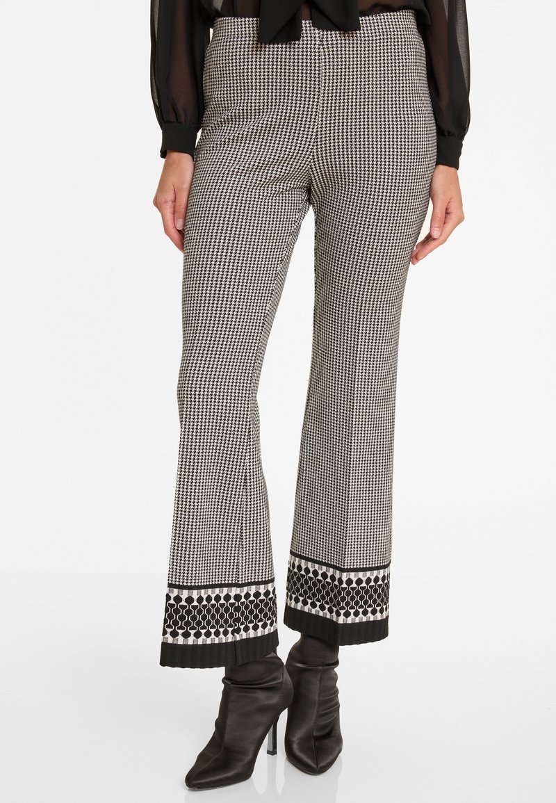 Schwarz-weiße Hahnentritt-Hosen mit ausgestelltem Schnitt und dekorativem gemustertem Saum, kombiniert mit schwarzen Stiefeletten. Glatte Stofftextur.