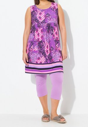 Femme portant une tunique sans manches à motifs violets et roses avec un ourlet rayé, des leggings violet clair et des sandales grises ouvertes à enfiler.