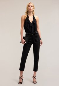 Black halter top with ruffles, high-waisted black trousers, and black strappy heels. Accessories include a black clutch and a wide belt.