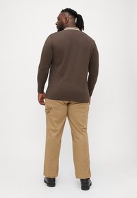 Brown long-sleeve polo shirt with a white collar, paired with khaki pants featuring side pockets and black boots.