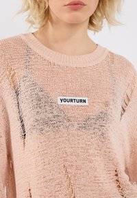 Kerge roosa kudum, millel on kulunud detailid ja ümar kaelus. Esiküljel on must "YOURTURN" silt.