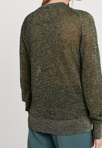 Pull en tricot de couleur vert foncé avec des fils métalliques, col rond, manches longues, poignets et ourlet côtelés, présentant une texture semi-transparente.