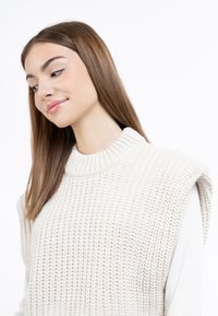 Pulover tricotat crem cu guler înalt cu nervuri și mâneci căzute, având un model texturat și un material moale.