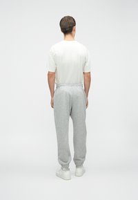 Svijetlosive trenirke s elastičnom trakom u struku i na rukavima, uparene s običnom bijelom majicom, prikazane sa stražnje strane.