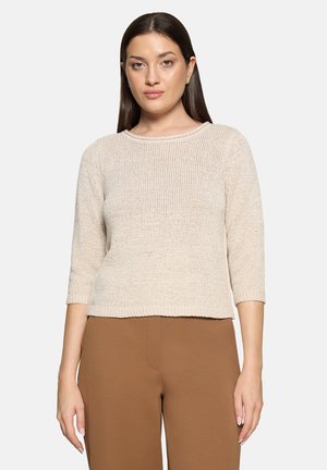 Pull beige en tricot avec un col rond, des manches trois-quarts et une coupe décontractée. Associé à un pantalon marron.