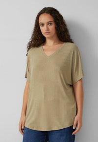 Khaki V-hals t-shirt met korte mouwen, voorzien van een ribbeltextuur en een relaxte pasvorm, gecombineerd met blauwe spijkerbroeken.
